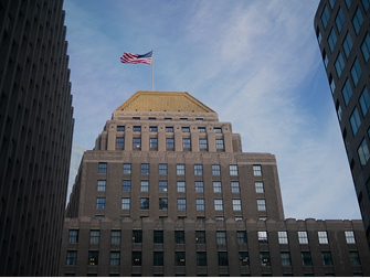 American flag flying atop a domed high-rise building between two skyscrapers
